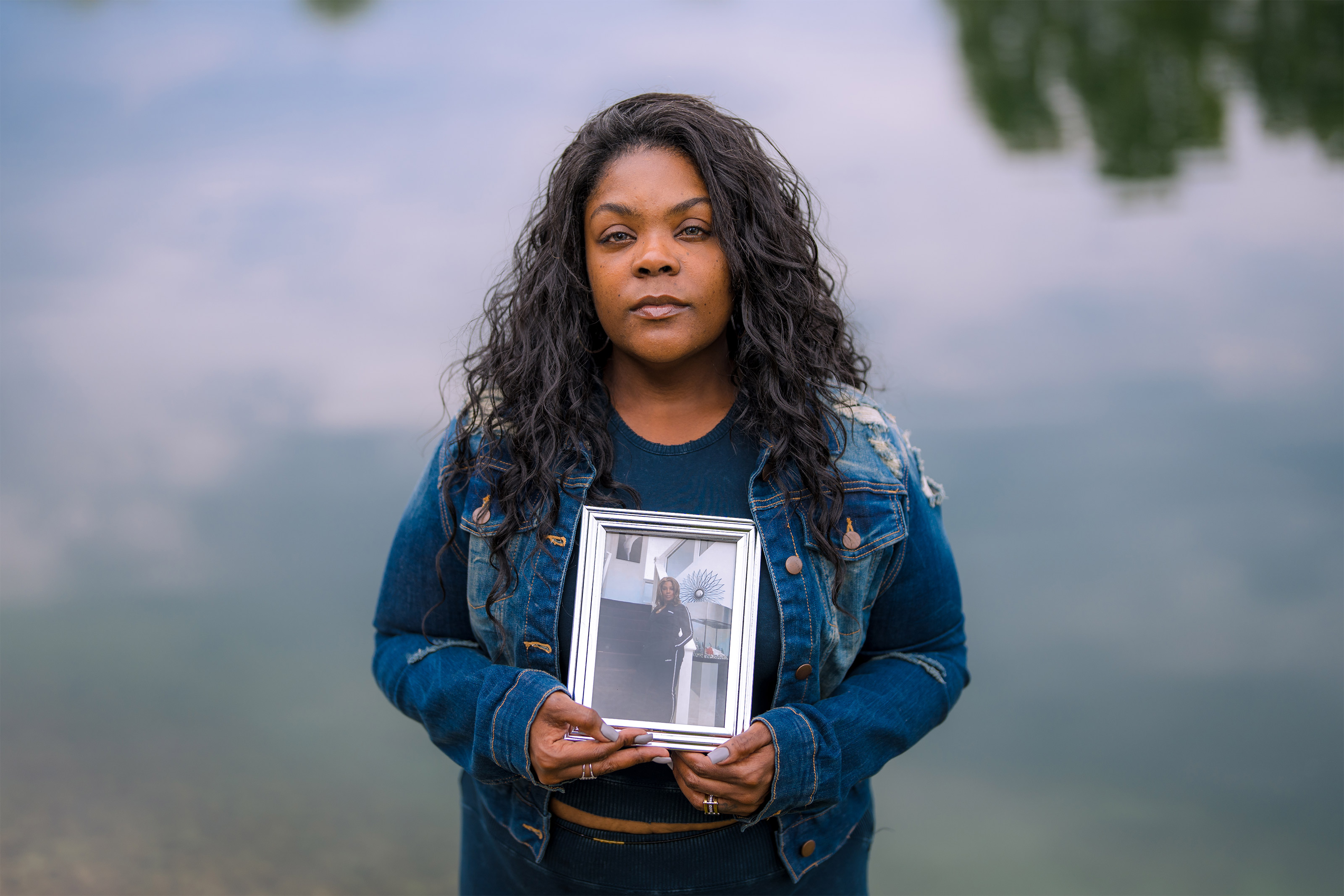 A photo of Ballard by water holding a framed picture of her mother.
